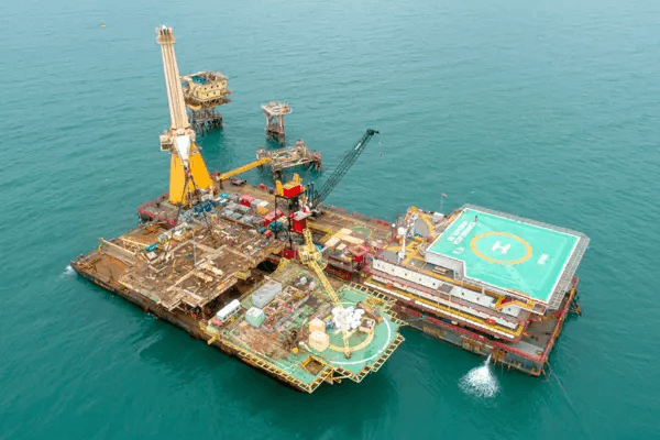 Photo of a Petrobras offshore platform being removed from the sea by a vessel with a crane.