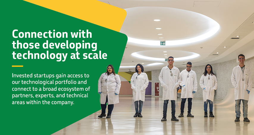 A group of six researchers in white lab coats posing in a modern laboratory corridor.