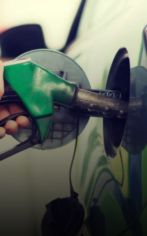 Hand holding a green fuel nozzle refueling a car at a gas station.
