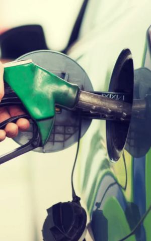 Hand holding a green fuel nozzle refueling a car at a gas station.