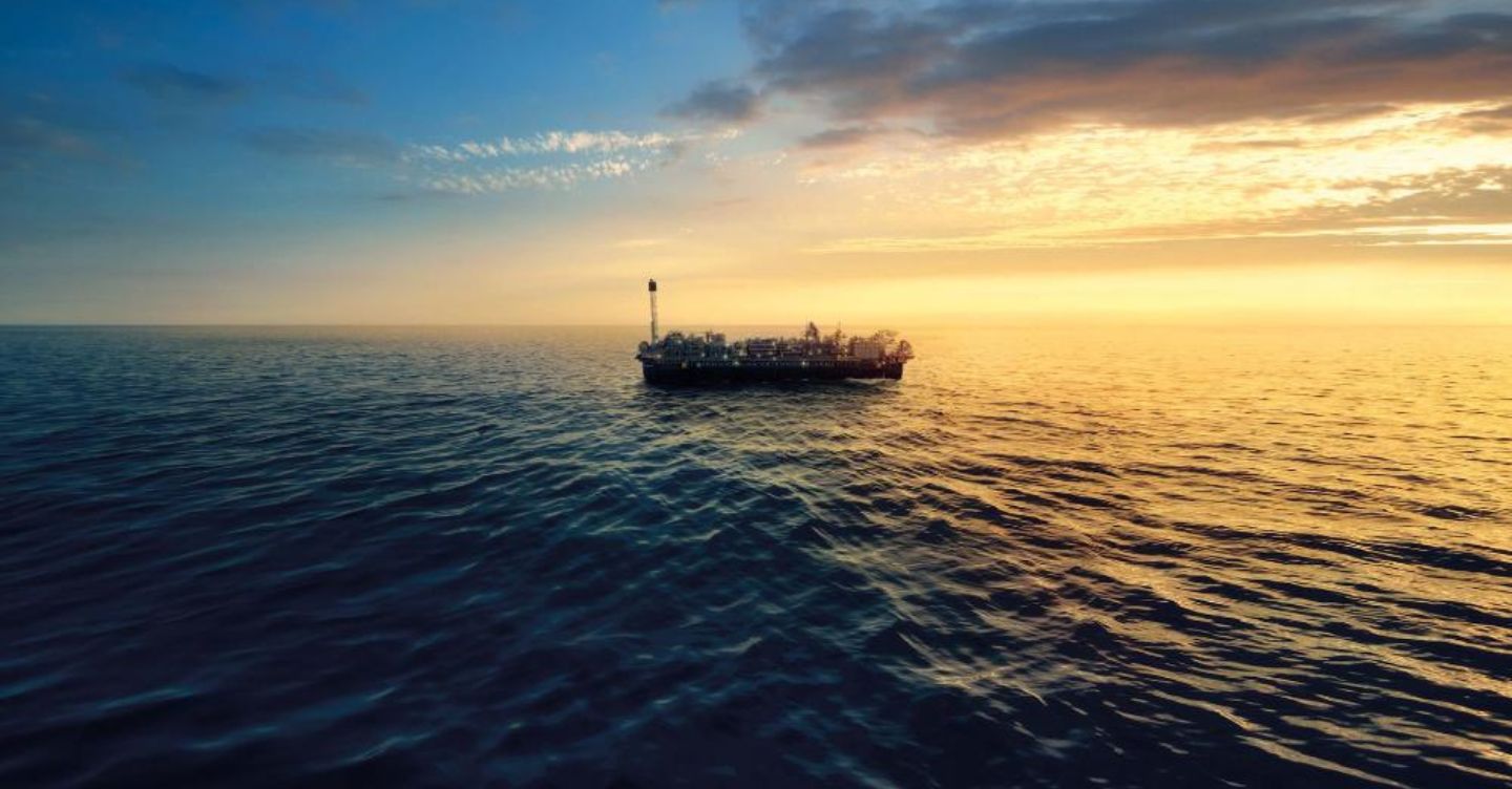 Offshore oil platform at sea during sunset, with an orange sky reflecting on the surrounding ocean.