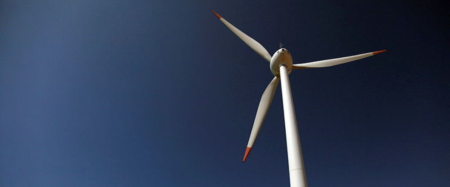 A wind turbine bearing the Petrobras logo, photographed from a low angle against a blue sky, symbolizing the company's investments in renewable energy.