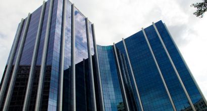 View from below of two corporate buildings with mirrored blue glass facades reflecting the cloudy sky.