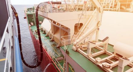 Operação de abastecimento entre embarcações no mar, com mangueiras conectadas para transferência de combustível e estruturas navais visíveis no convés.