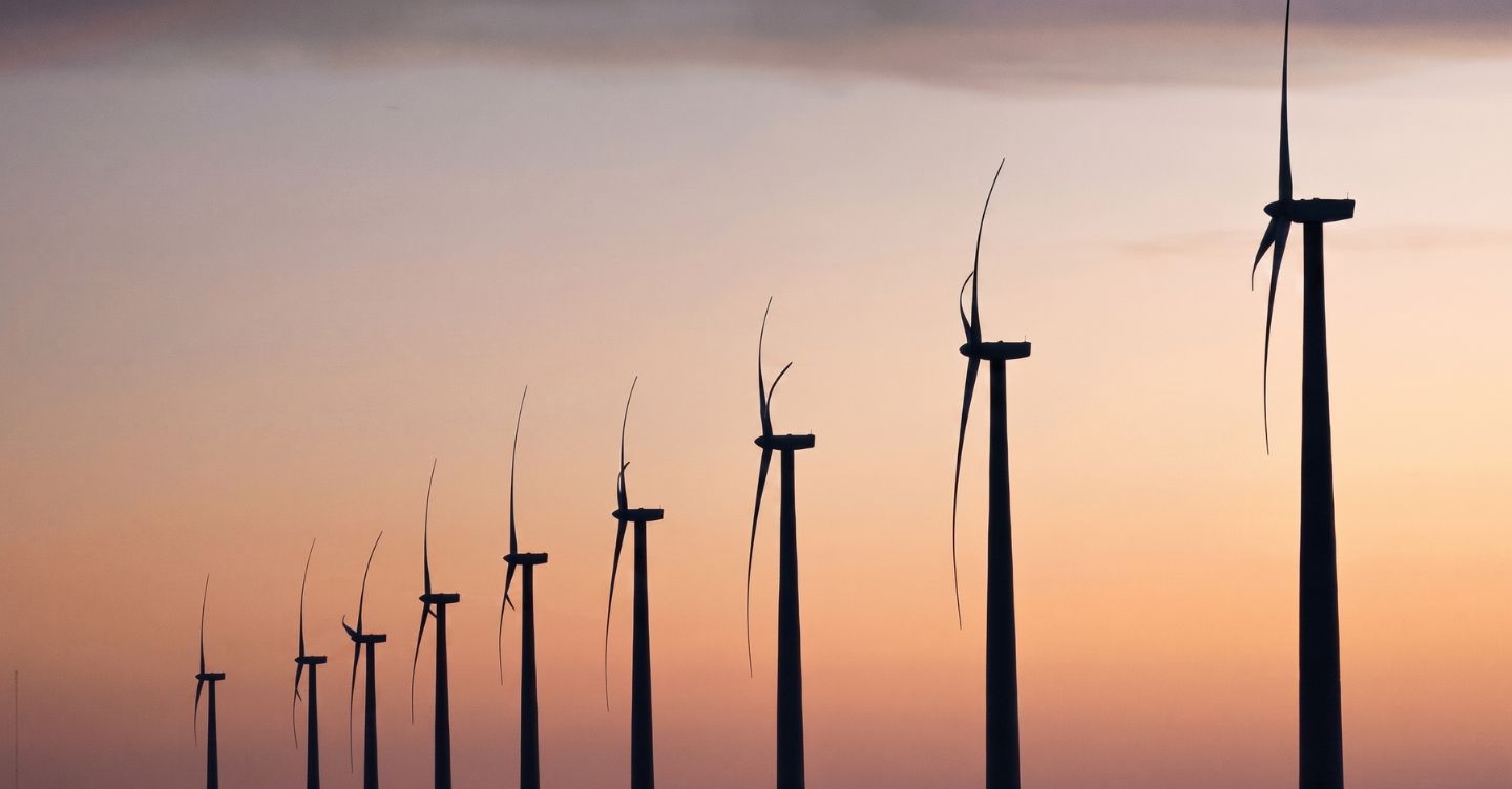 Fileira de turbinas eólicas em silhueta ao pôr do sol com texto "A importância das energias renováveis".