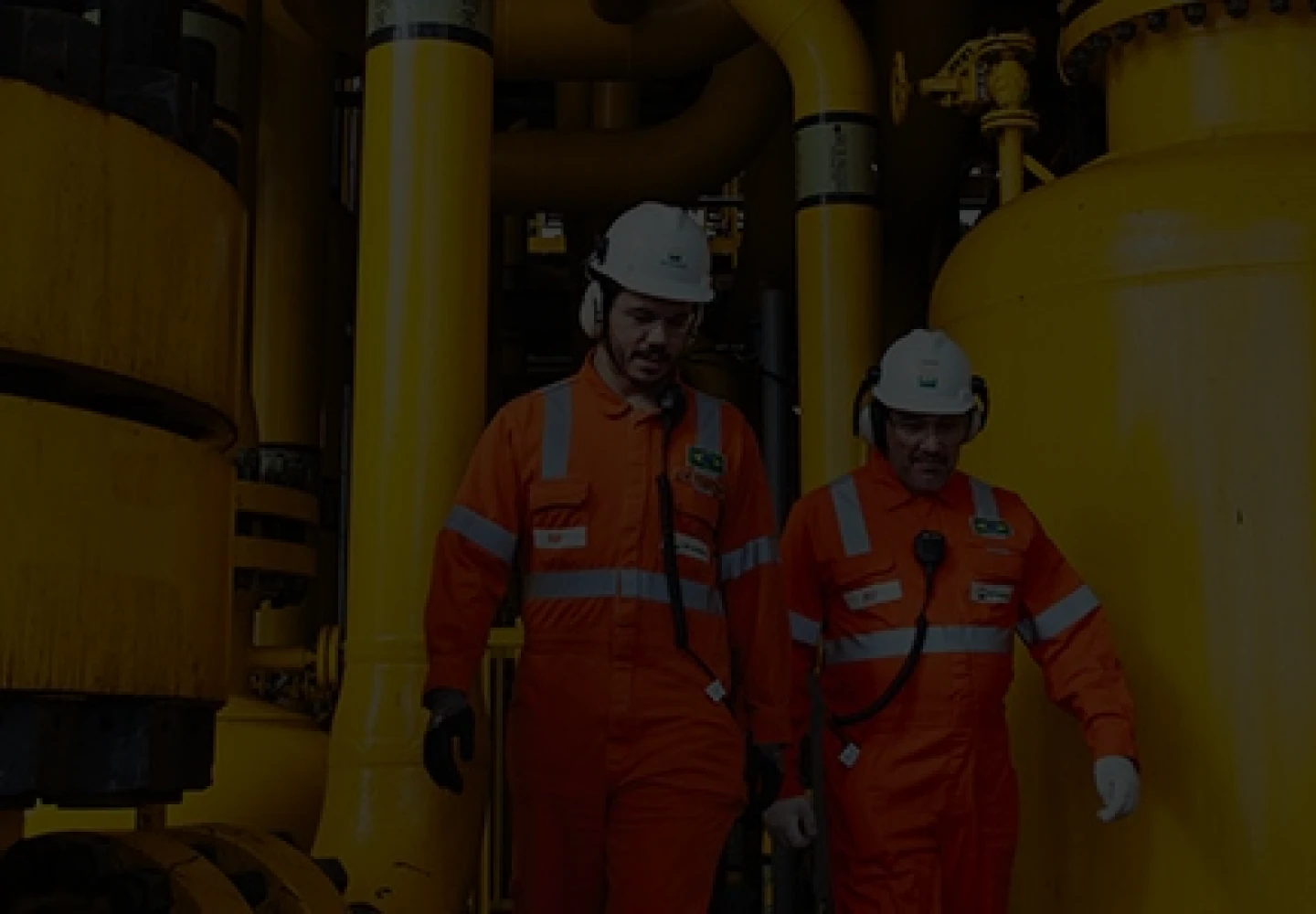 Colaboradores Petrobras vestindo EPIs de segurança enquanto trabalham em refinaria.