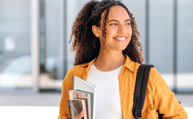Estudante morena sorrindo e olhando para o lado segurando livros e apostilas