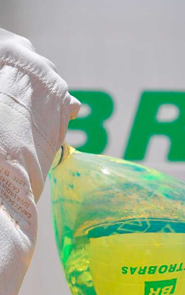 Mão com luva branca segurando vidro com amostra de diesel R5.