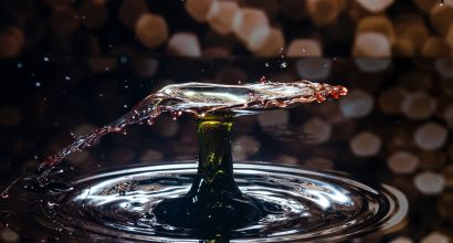 Water droplet forming a crown splash on the surface, with reflections and blurred lights in the background.