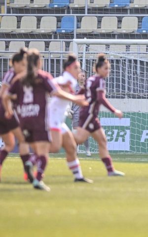 Players contest the ball during a women’s soccer match in a stadium.