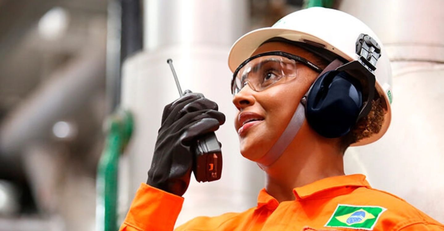 Worker wearing PPE in an industrial setting, speaking into a radio communicator.