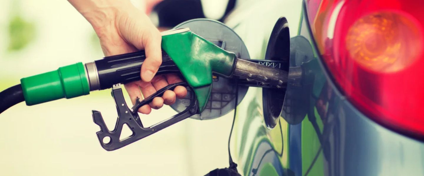 Hand holding a green fuel nozzle refueling a car at a gas station.