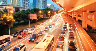 Heavy traffic on an urban avenue at dusk, with illuminated buildings and car light trails.