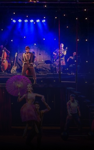 Stage performance with musicians and circus performers under colorful lights.