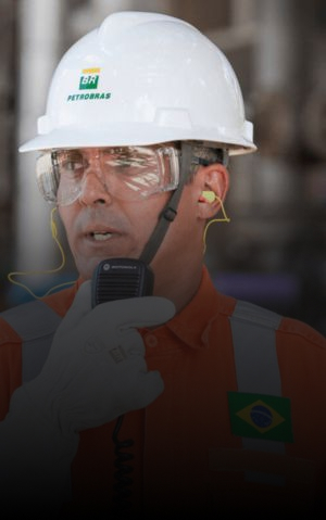 Worker wearing PPE in an industrial setting speaking into a radio communicator.