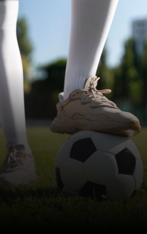 Player with foot on a soccer ball on a field, with other athletes in the background.