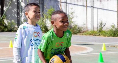 Two smiling children on a sports court, one holding a ball, during an outdoor activity.