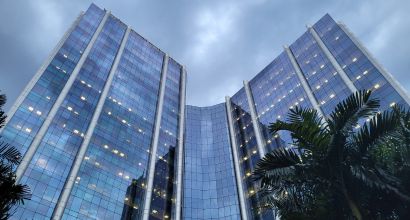 Low-angle view of Petrobras headquarters building in Rio de Janeiro, a glass-facade tower reflecting the cloudy sky, surrounded by palm trees.