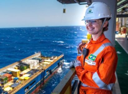 Mulher sorrindo em uma plataforma de petróleo no mar, usando uniforme laranja da Petrobras.