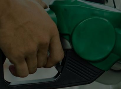 Pessoa abastecendo um carro, com destaque para a mão segurando o bico de abastecimento.