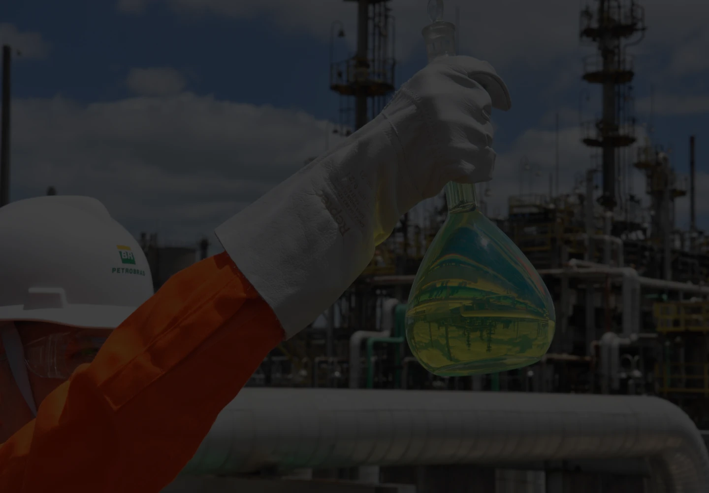 Photo of a Petrobras employee holding a glass with fuel inside, in front of a refinery.