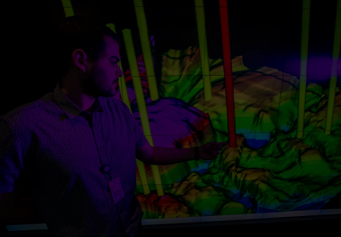 Fotografia de um homem observando uma modelagem 3D de um terreno sendo projetada em uma parede.
