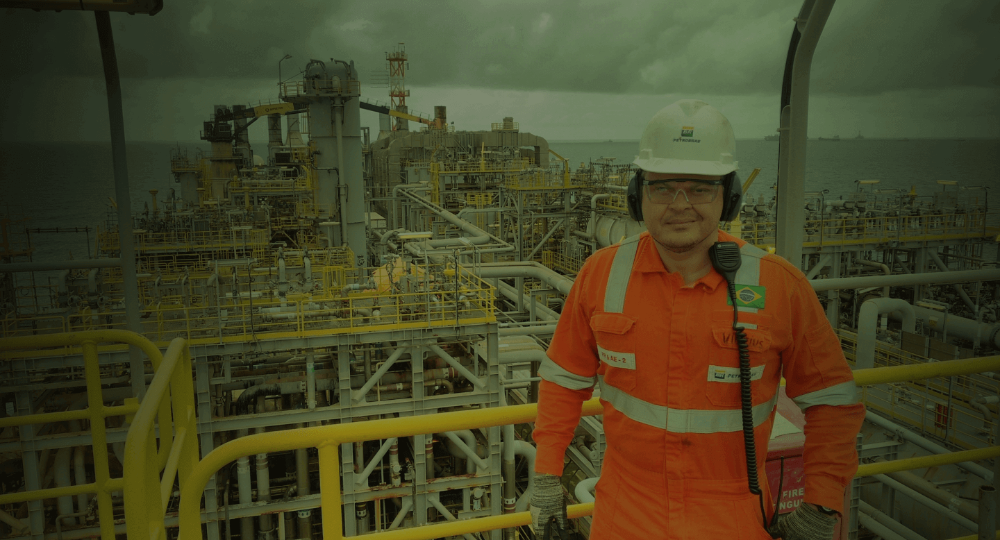 Funcionário com carreira na Petrobras, usando uniforme, em frente a plataforma marítima.