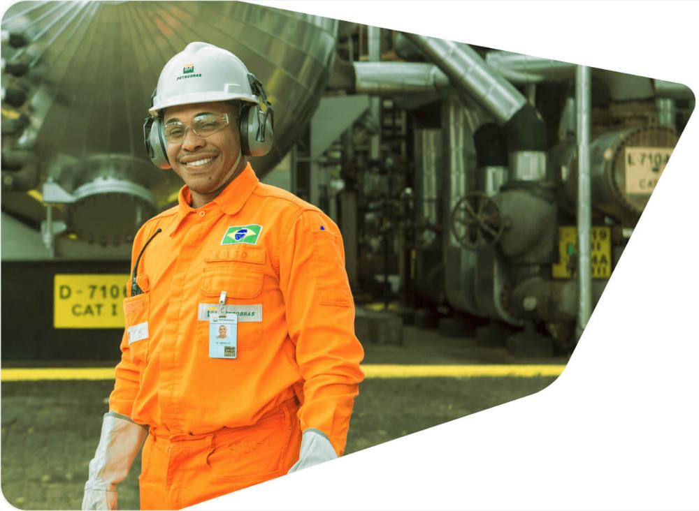 Funcionário com carreira na Petrobras sorri para a câmera, usando uniforme e equipamento de proteção completo.