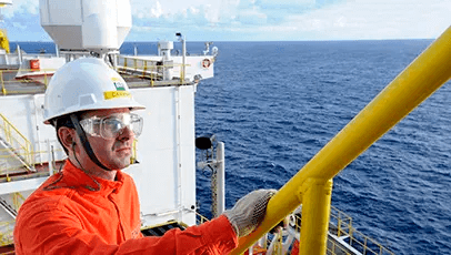 Two Petrobras employees wearing safety gear. One of them fixes the other's helmet.