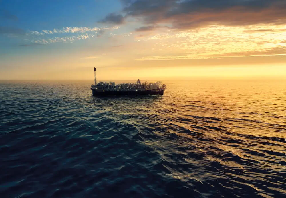 Fotografia de uma plataforma FPSO da Petrobras durante o nascer ou pôr do sol.