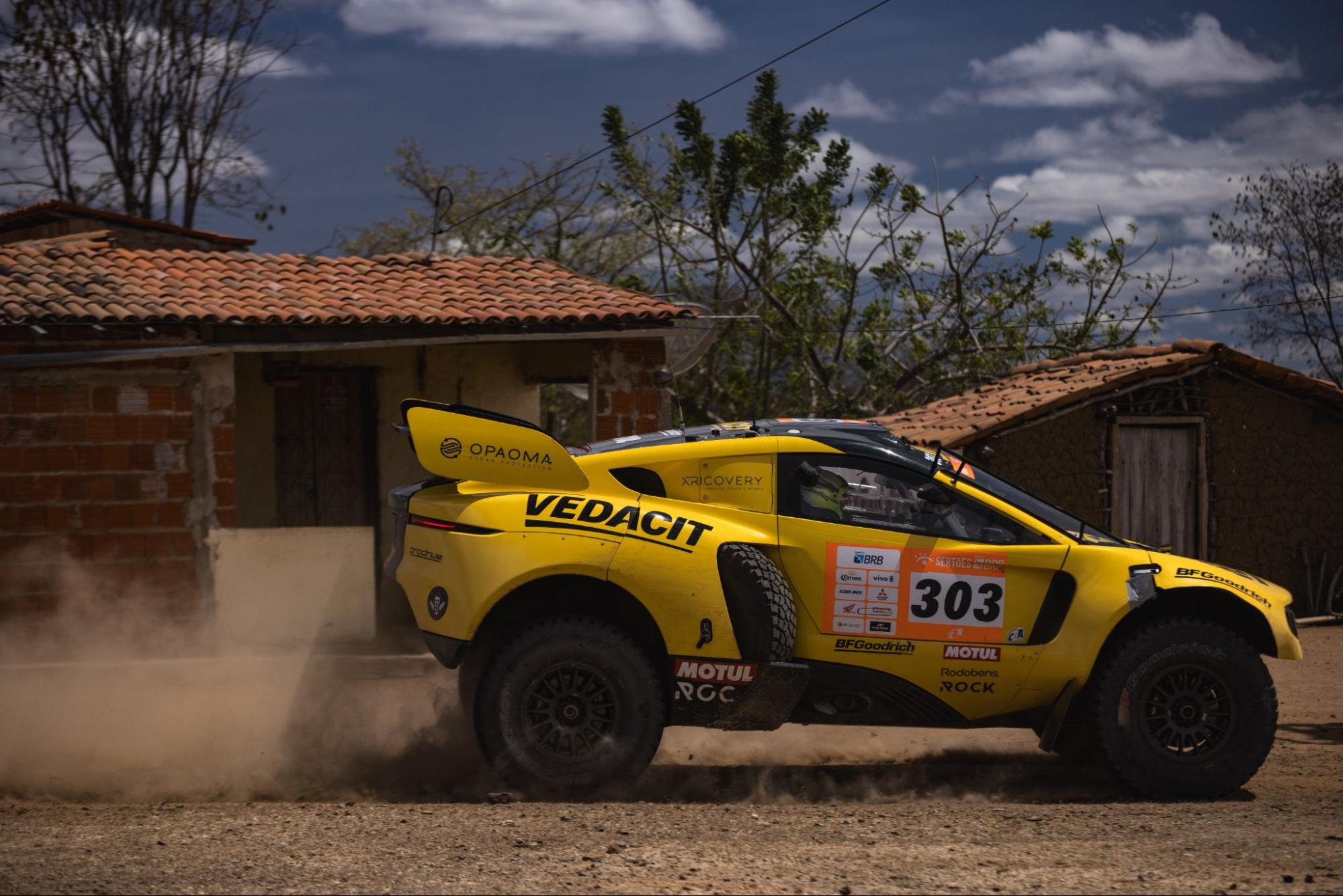 Competitor car passes in front of a typical house in the Brazilian backlands