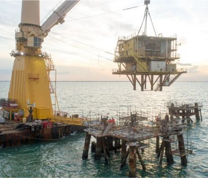Foto de uma plataforma offshore da Petrobras sendo retirada do mar por uma embarcação com guindaste.