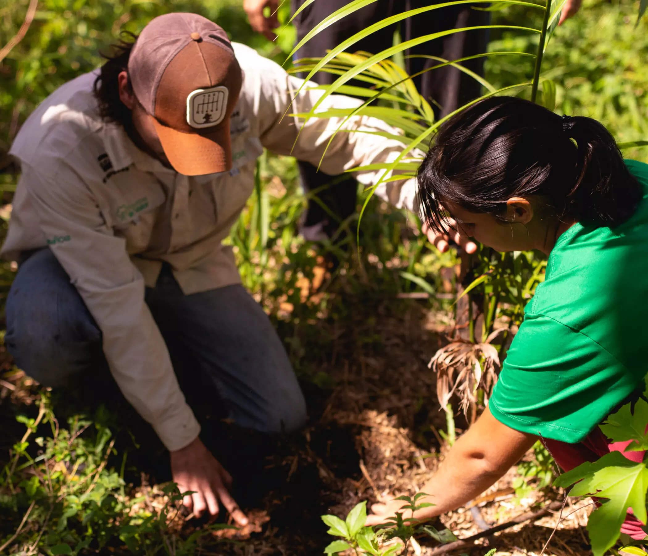 Man and woman touching their hands to the floor of the Amazon rainforest. Both wear clothes from the “Florestas de Valor” Project, supported by Petrobras.