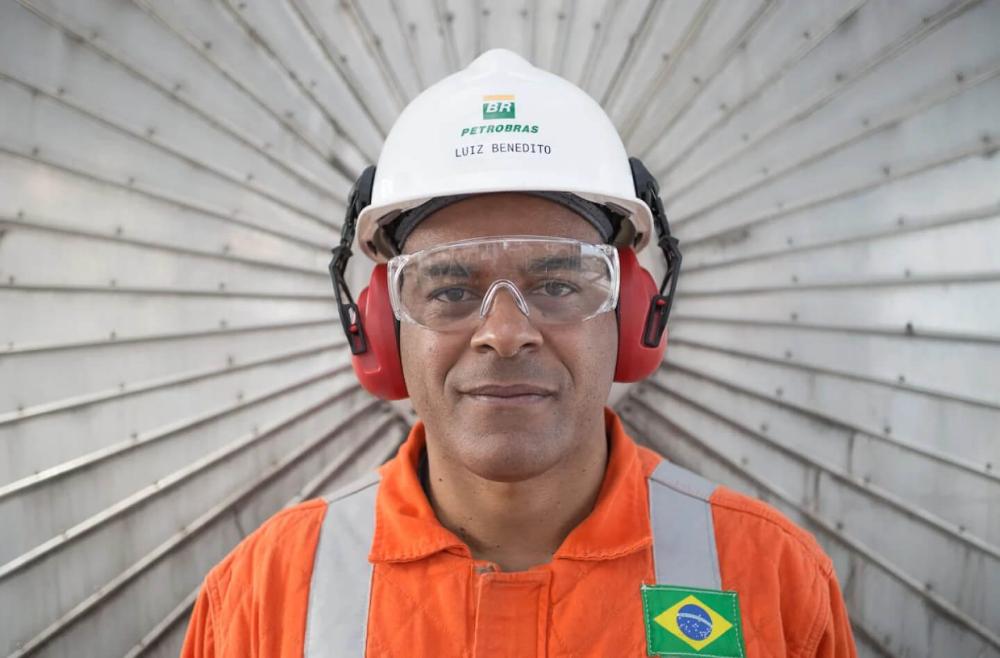 Funcionário da Petrobras olha diretamente para a câmera. Em seu capacete está a marca Petrobras.