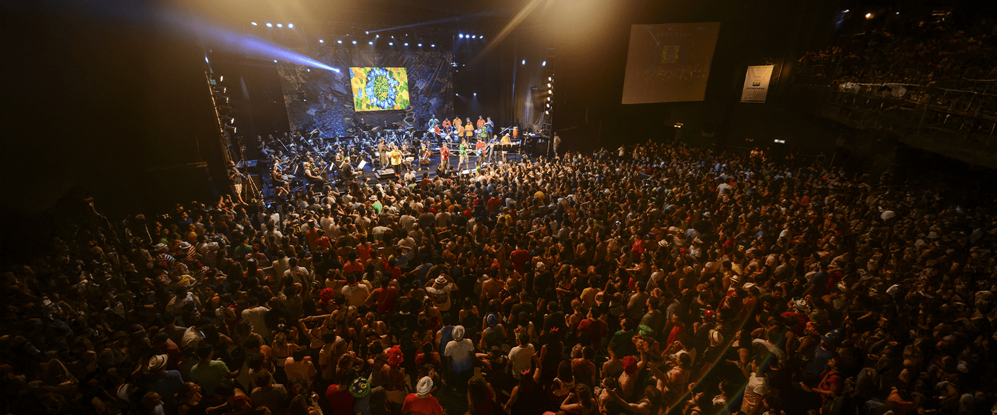 Monobloco concert at Fundição Progresso, with a large crowd and full orchestra on stage.