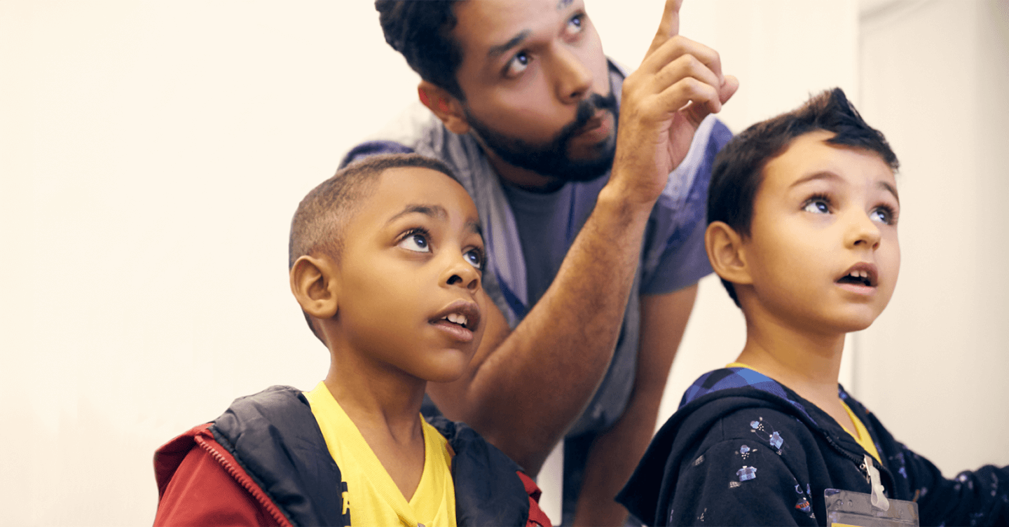 Man guiding two curious children as they look and point toward something, symbolizing education and inspiration.