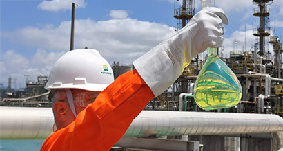 Petrobras employee holding glassware with R Diesel inside, in front of a refinery.