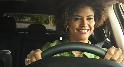 Close up of a smiling woman holding a steering wheel.