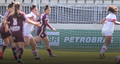 Women playing soccer on a field with a Petrobras sign in the background.