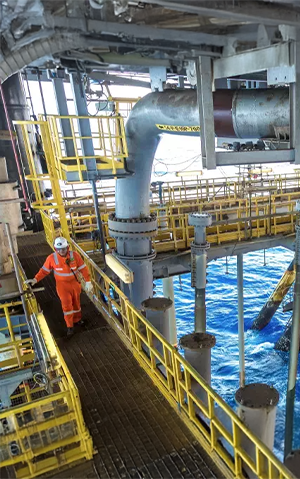 Offshore oil platform with a worker in safety gear walking along a metal walkway above the ocean.