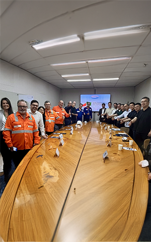Participantes do Fórum Estratégico Brasil-China para a Indústria Naval reunidos em sala de reunião, posando em frente a uma mesa com sinal de positivo.
