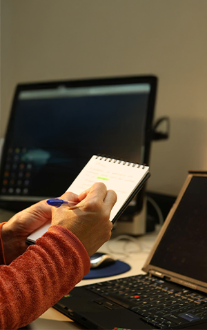 Mulher fazendo anotações em bloco diante de notebook.