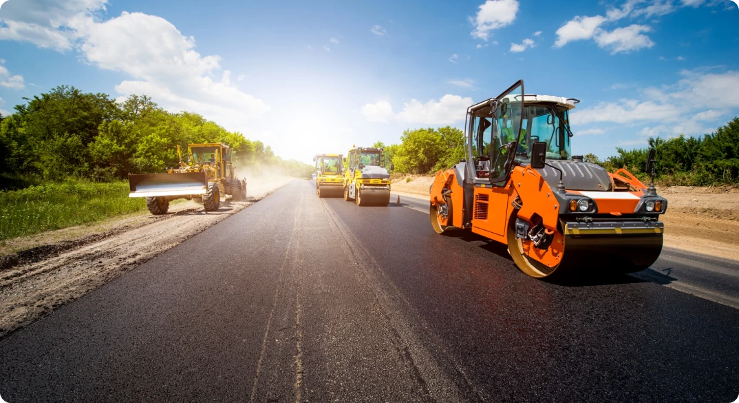 Daytime photo of four road machines paving a road with asphalt products.