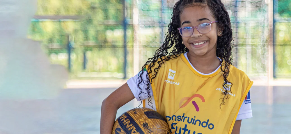 Menina de óculos segurando bola de vôlei. Ela faz parte do time Petrobras Construindo O Futuro.
