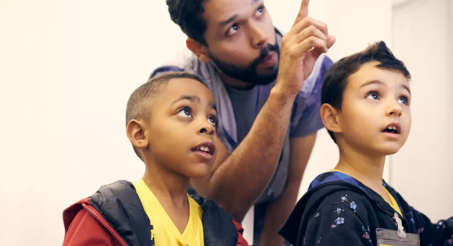 An adult pointing at something while talking to two children.