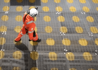 Aerial photo of a Petrobras employee walking on a metallic floor grid, wearing protective gear.