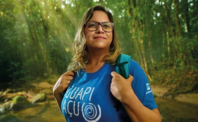 Mulher loira de óculos na floresta com camisa do Projeto Guapiaçu