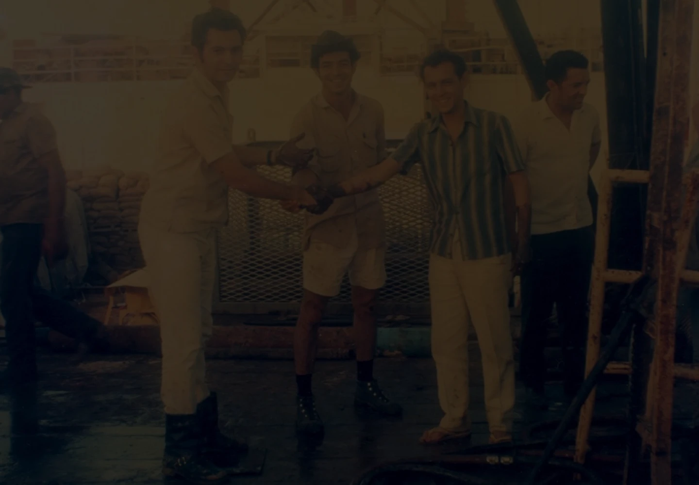 Old photo of three men greeting each other as they look at the camera on a platform in the Guaricema field.